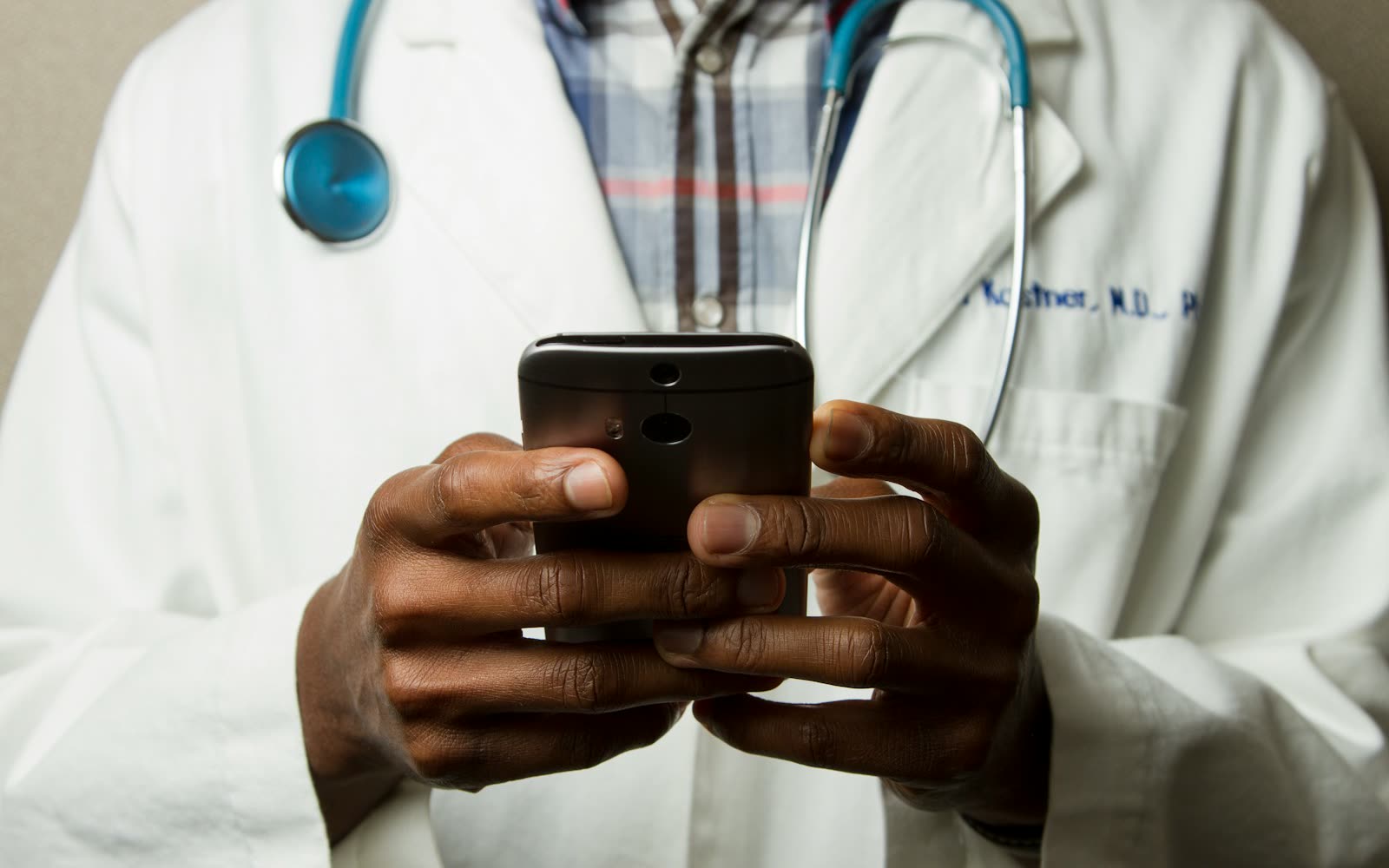 A physician in a white coat reading a message on their phone