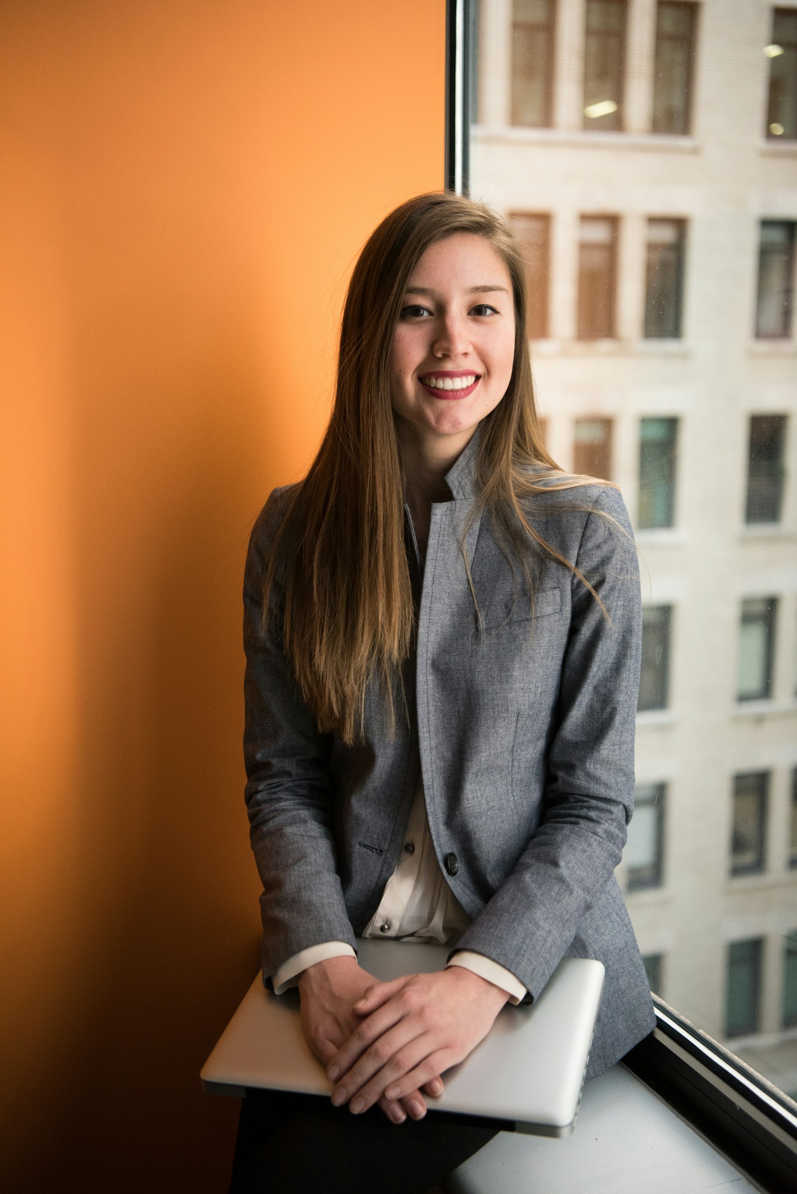 A smiling young professional holding a laptop in an office